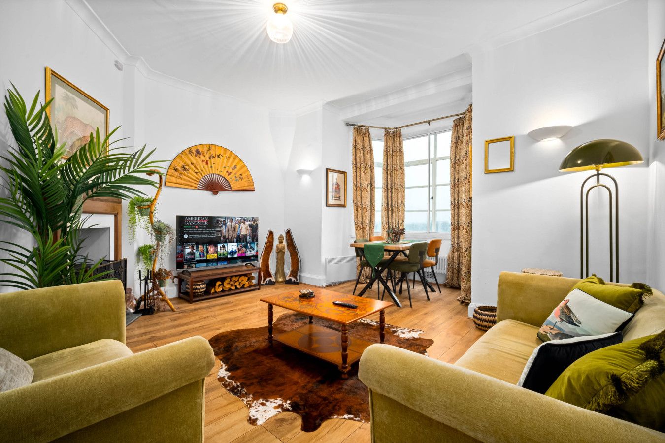 A living room with a wooden coffee table, two green armchairs, a sofa, a TV, and a dining area with a table and chairs.