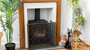 Ein Zimmer mit einem schwarzen Metall-Kamin, einem hölzernen Kaminvorsatz und einer Topfpflanze.