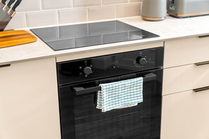 Una cocina con un horno negro, un reloj digital y una tabla de cortar de madera sobre la encimera.