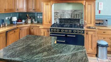 Una cocina con armarios de madera, encimera de granito, estufa y un cubo de basura.