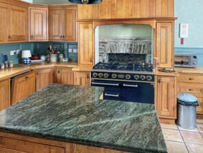 A kitchen with wooden cabinets, a granite countertop, a stove, and a trash can. - Bailiffs House - UK48744 (Llandybie)