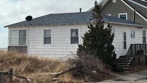 Una casa de un piso con techo gris, una chimenea y un cartel de 'RENT' en la ventana.