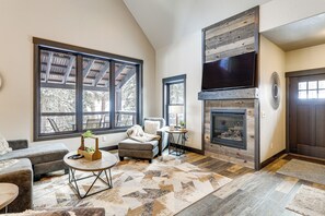 A living room with a fireplace, large windows, a sofa, and a coffee table. - Hot Tub + Deck: Secluded Black Hills Retreat! (Lead)