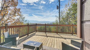 Eine Holzterrasse mit Gartenmöbeln, Blick auf Bäume und Berge, und ein klarer Himmel.