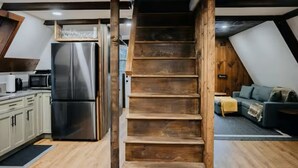 A modern kitchen with a stainless steel refrigerator, wooden staircase, and a living area with a sofa and a fireplace. - Cozy & Modern A-Frame in the woods w/HOT TUB (Tamworth)