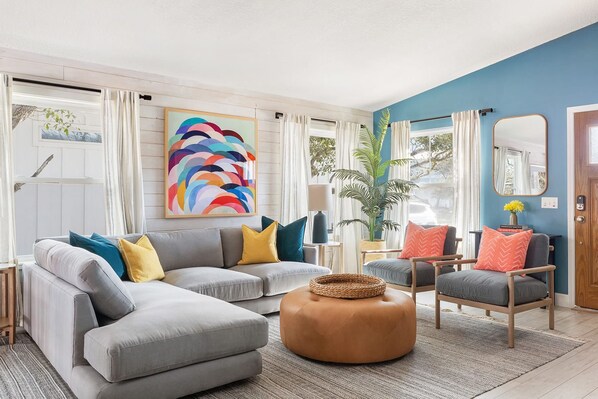 Relax in this stylish living room with a grey sofa, colorful throw pillows, and a large abstract painting.