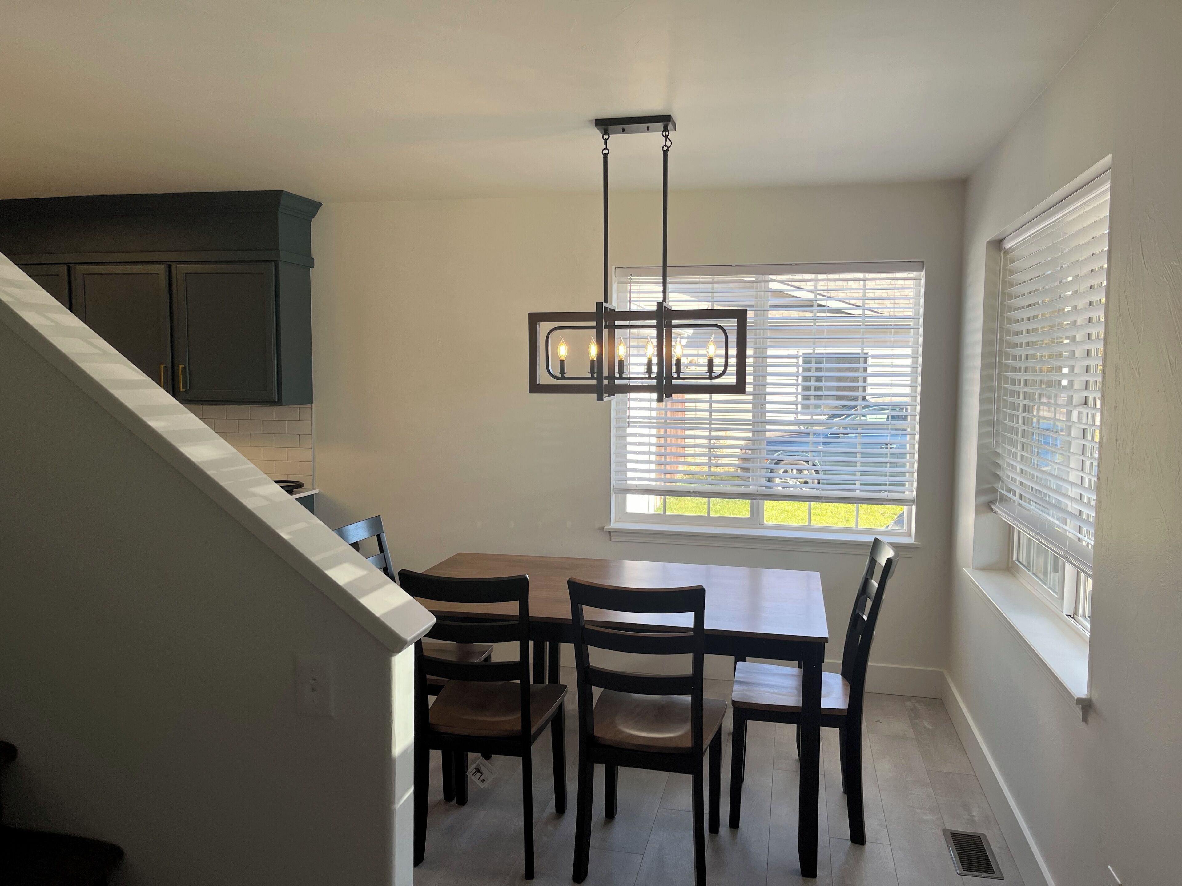 Un coin repas comprenant une table et des chaises, un luminaire suspendu et une fenêtre avec des stores.