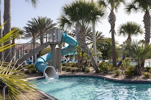 A water slide leading into a pool surrounded by palm trees and a covered seating area. - Orlando Resort Retreat Resort Home With Pool Arcade Kids Will Love (Davenport)