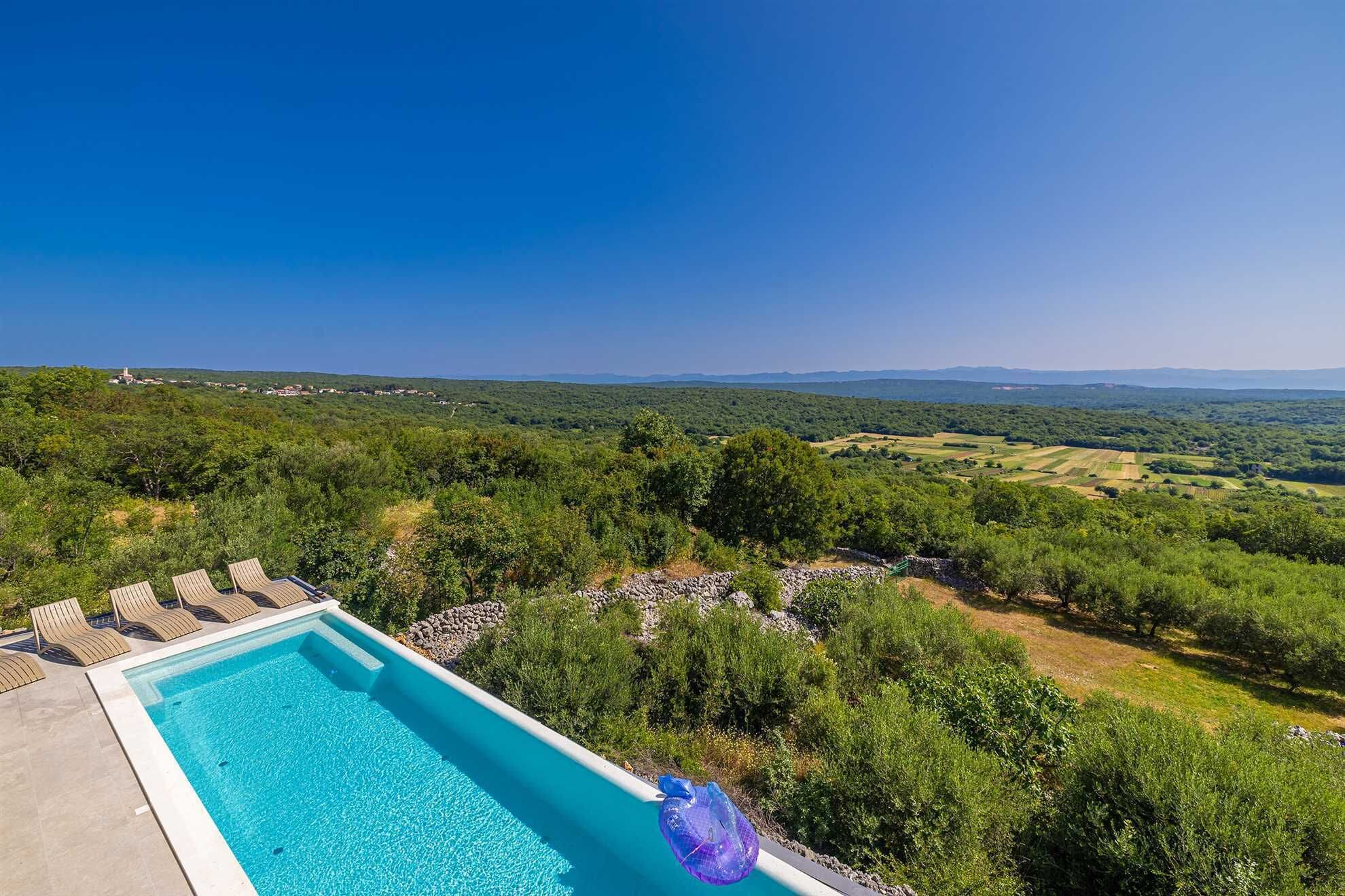 Una piscina con sillones de descanso y vistas a un paisaje verde con colinas al fondo.