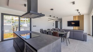 Una cocina moderna con una isla central, zona de comedor con sofá y un televisor montado en la pared.