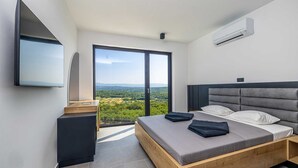 Un dormitorio moderno con una cama grande, un televisor montado en la pared y vistas al campo a través de una puerta corredera.