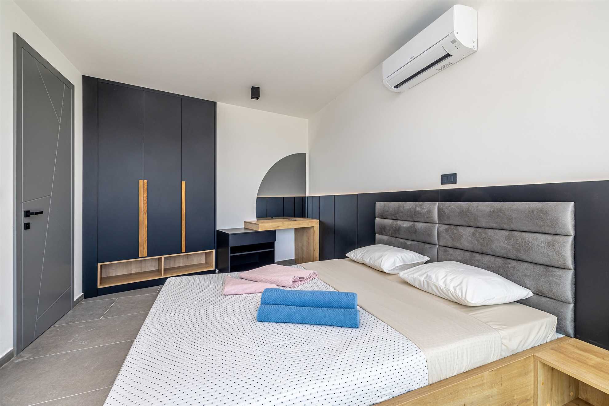 A modern bedroom with a bed, a wardrobe, a desk, and an air conditioning unit.