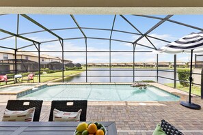 A covered outdoor area with a pool, lounge chairs, and a view of a lake. - Twice-as-nice Resort Home Near Disney Pool and Game Room 20 Guests (Kissimmee)