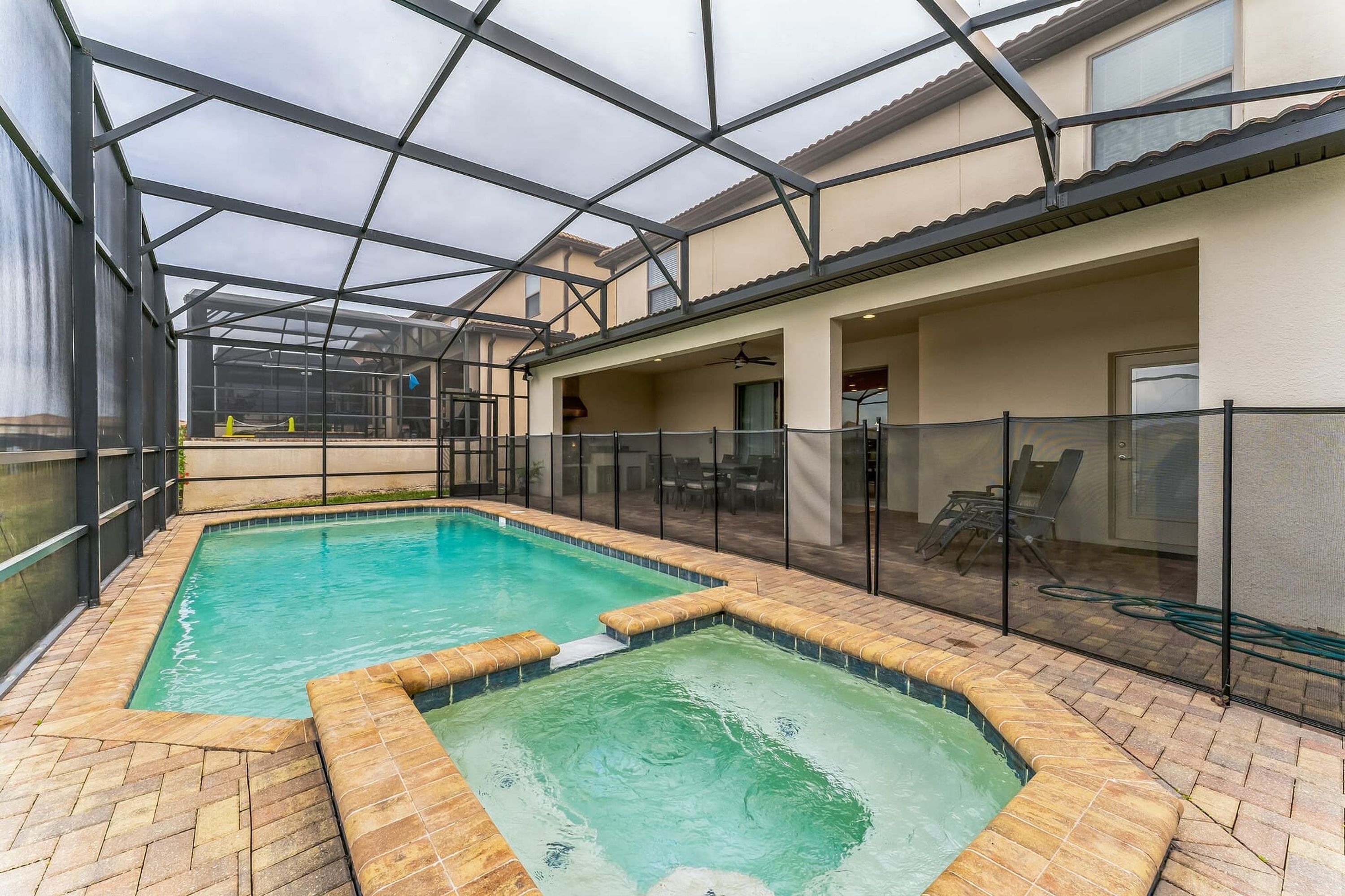 Una piscina con cerramiento de vidrio, rodeada por un patio de ladrillo y una valla de vidrio.