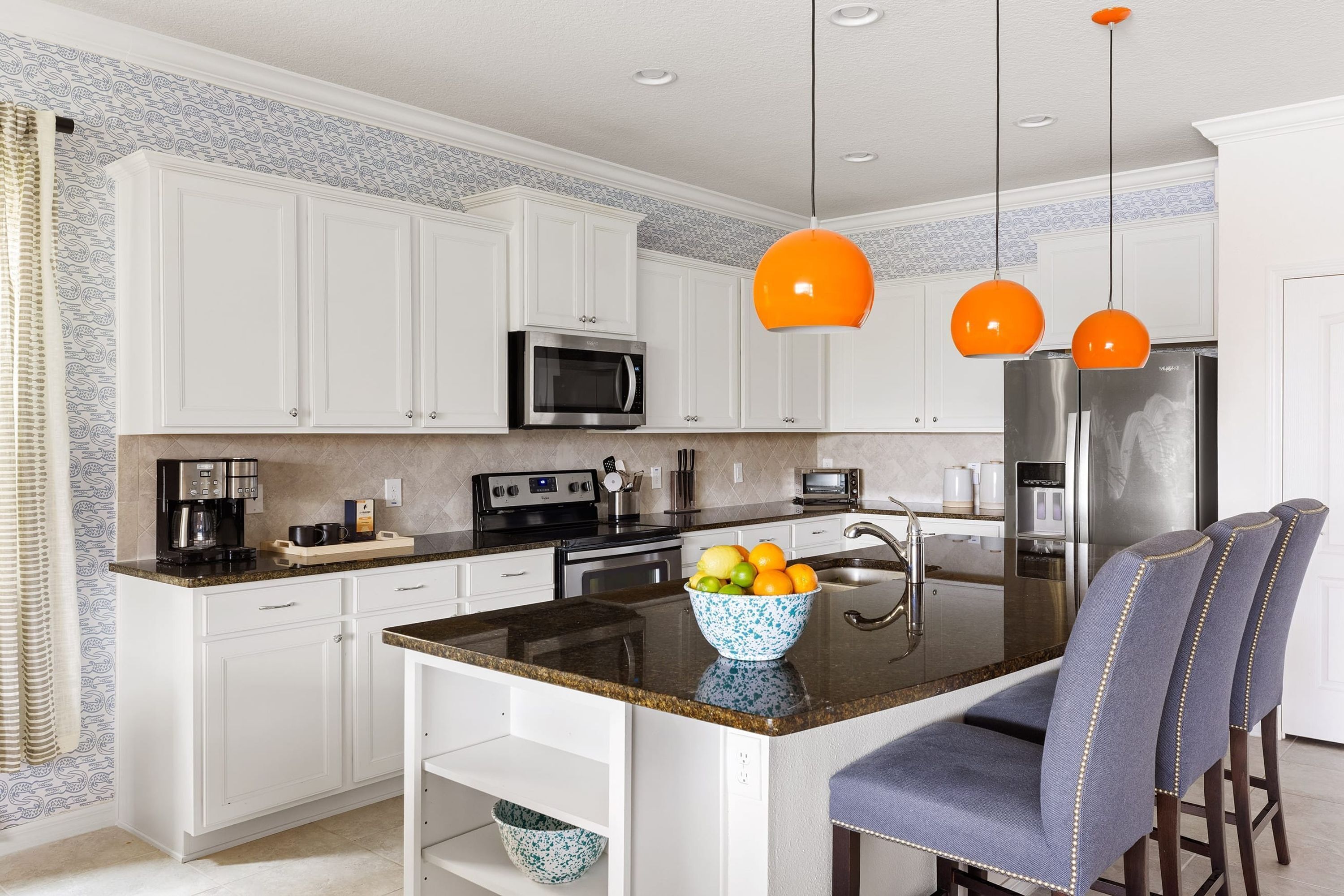 A modern kitchen with white cabinetry, a granite countertop, a stainless steel refrigerator, and a fruit bowl on the island.