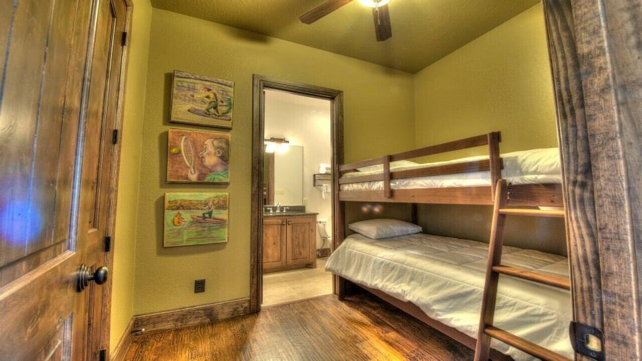 A room with a bunk bed, wooden flooring, a door, and a mirror.