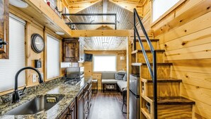 Une cuisine compacte dotée de plans de travail en granit, d’un évier et d’une cuisinière. On aperçoit un escalier en bois et une fenêtre au fond.