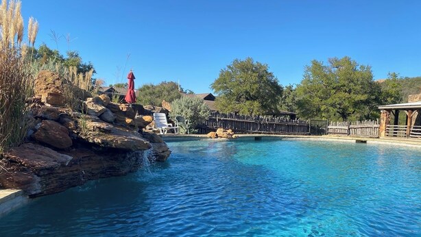 Une piscine aux eaux d’un bleu limpide, bordée de rochers, entourée d’arbres et d’une clôture en bois.