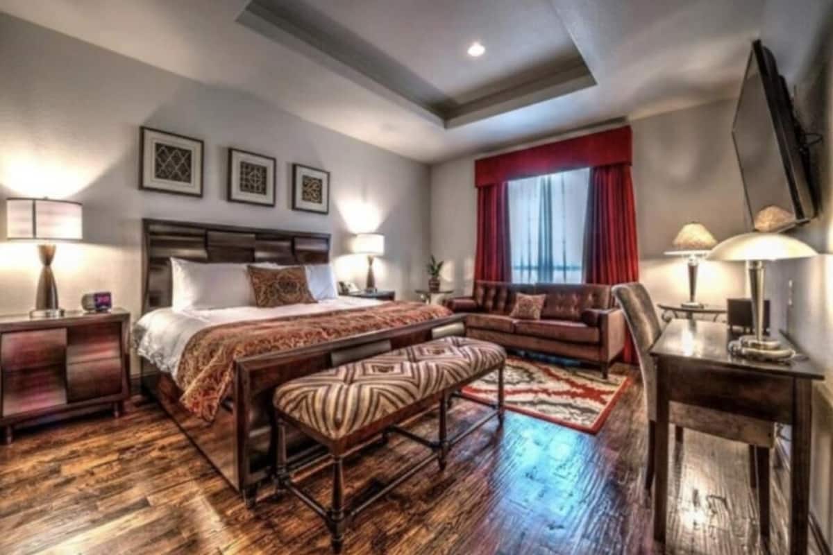 Ein Hotelzimmer mit einem großen Bett, einem Sofa, einer Bank, einem Schreibtisch und einem Fernseher.