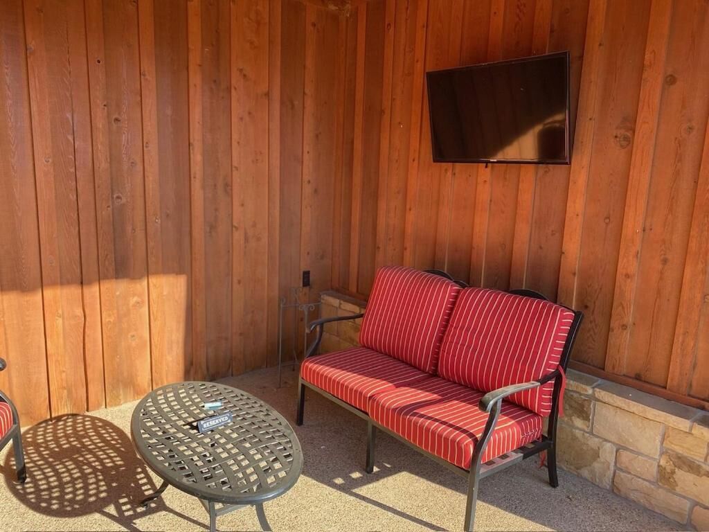 Pared de madera con un televisor de pantalla plana sobre un sofá rojo a rayas y dos mesas redondas.