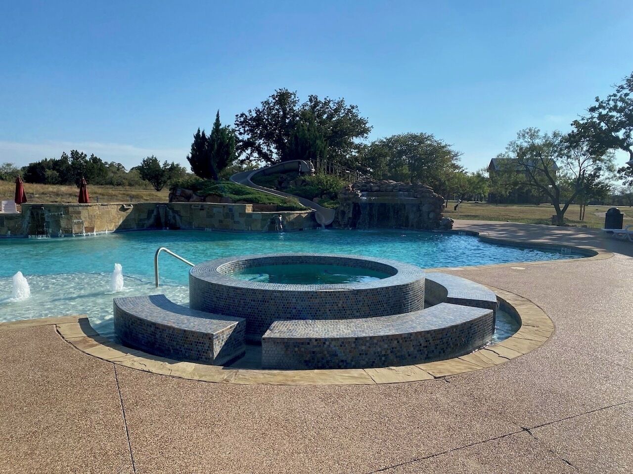 A pool with a circular hot tub and a stone pathway leading to it.