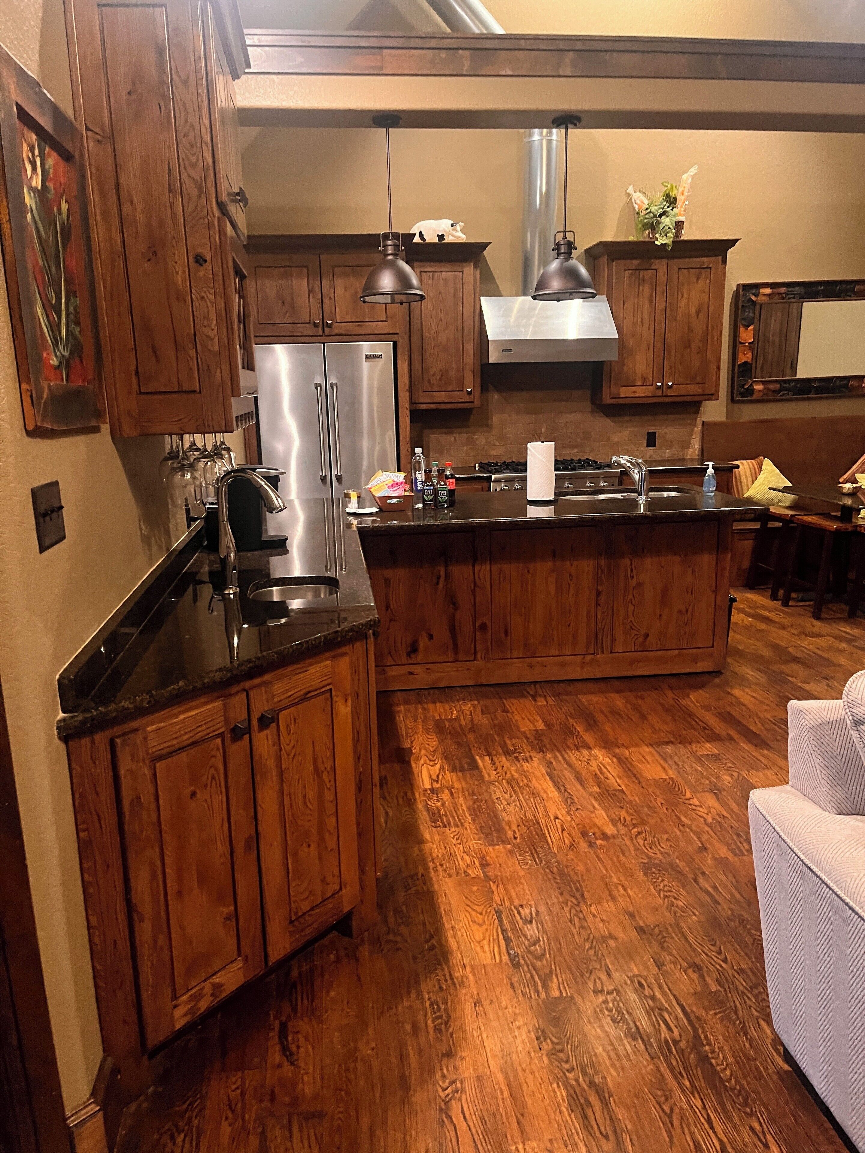 A kitchen with wooden cabinets, a stainless steel refrigerator, a large island with a sink, and hanging pendant lights.