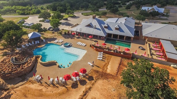 An aerial view of a resort with a swimming pool, lounge chairs, and a covered outdoor area.