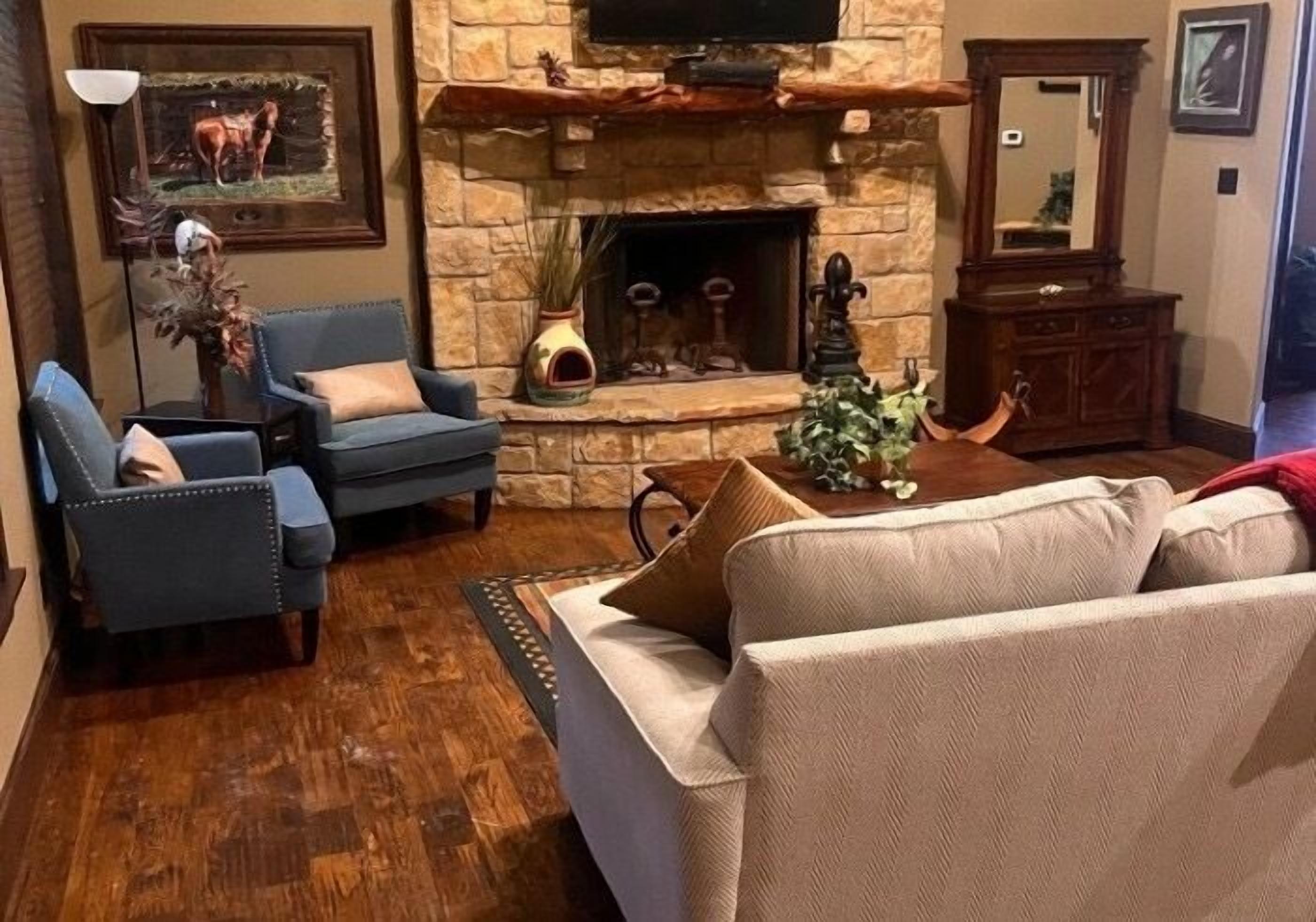 Una sala de estar con chimenea de piedra, sillones azules, un sofá beige y una mesa de centro de madera.