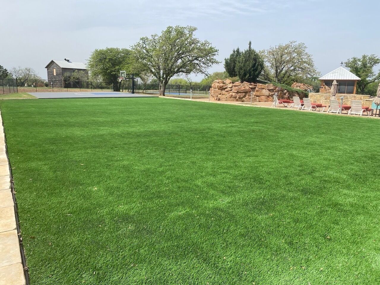A well-maintained lawn with a basketball court, a stone building, and a gazebo with seating.
