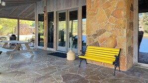 A covered patio area with stone flooring, a wooden bench, and a table with chairs.