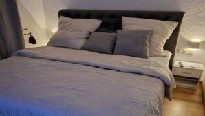 Un dormitori amb un llit gran, un capçal, una tauleta de nit amb una làmpada, i un quadre amb marc a la paret.