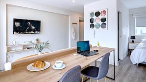 Une chambre d’hôtel moderne avec un bureau en bois, un ordinateur portable, un croissant et une tasse de café.
