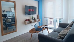 Un salon moderne avec un téléviseur à écran plat, un ordinateur portable posé sur une table basse en bois, un canapé et un grand miroir.