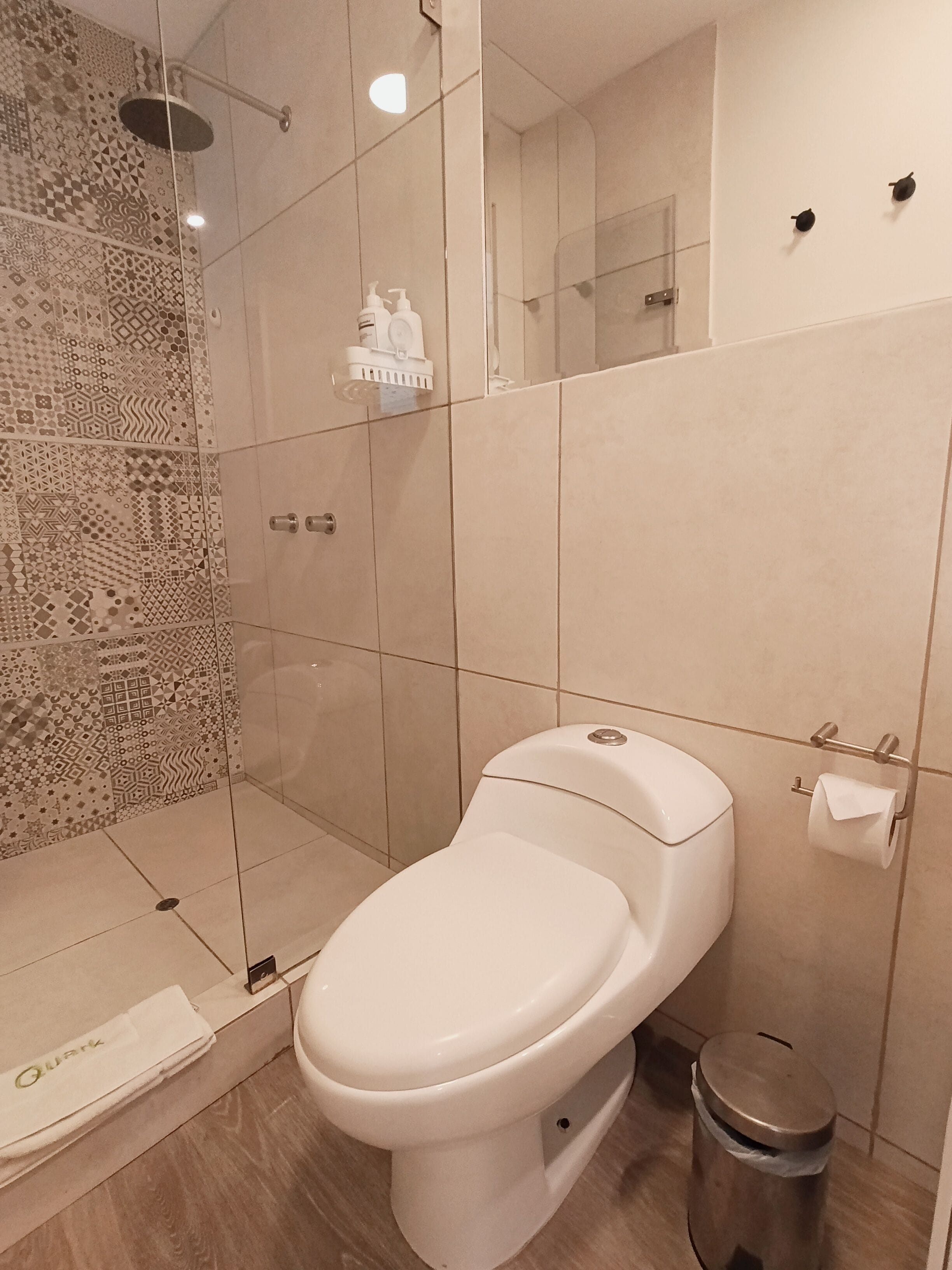 A modern bathroom with a toilet, a glass shower enclosure, and a patterned wall.