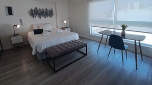 Une chambre à coucher moderne avec un lit, des tables de chevet, un banc, un bureau et une fenêtre.