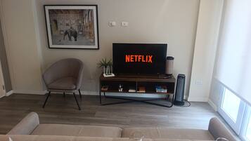 Una sala de estar moderna con un televisor de pantalla plana, un cuadro enmarcado, una silla, un sofá y una copa de vino.
