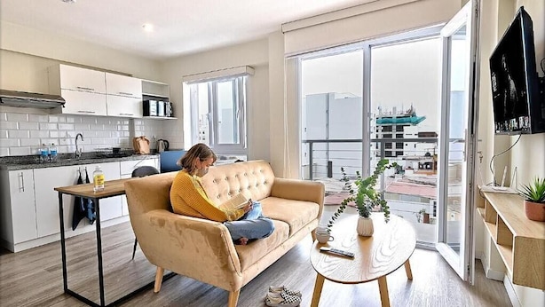 Un appartement moderne comprenant une cuisine, un espace de vie avec un canapé, une table à manger et une grande porte-fenêtre coulissante donnant sur un balcon.