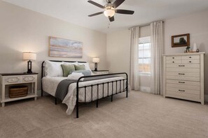 A bedroom with a bed, bedside tables, a dresser, a ceiling fan, and a window with curtains.