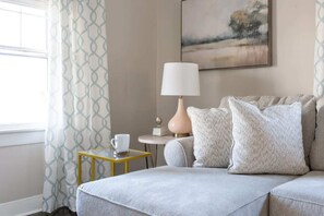 A room with a sofa, a small table with a cup, a lamp, and a painting on the wall.