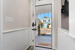 A hallway with a white door leading to a blue house with a chimney.