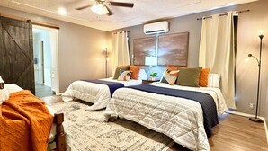 Une chambre d’hôtel avec deux lits, un ventilateur de plafond, un appareil de climatisation, un bureau avec une chaise et une grande fenêtre avec des rideaux.
