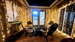 Un espace extérieur accueillant, aménagé avec une table ronde et des chaises, entouré de guirlandes lumineuses et de grandes fenêtres.
