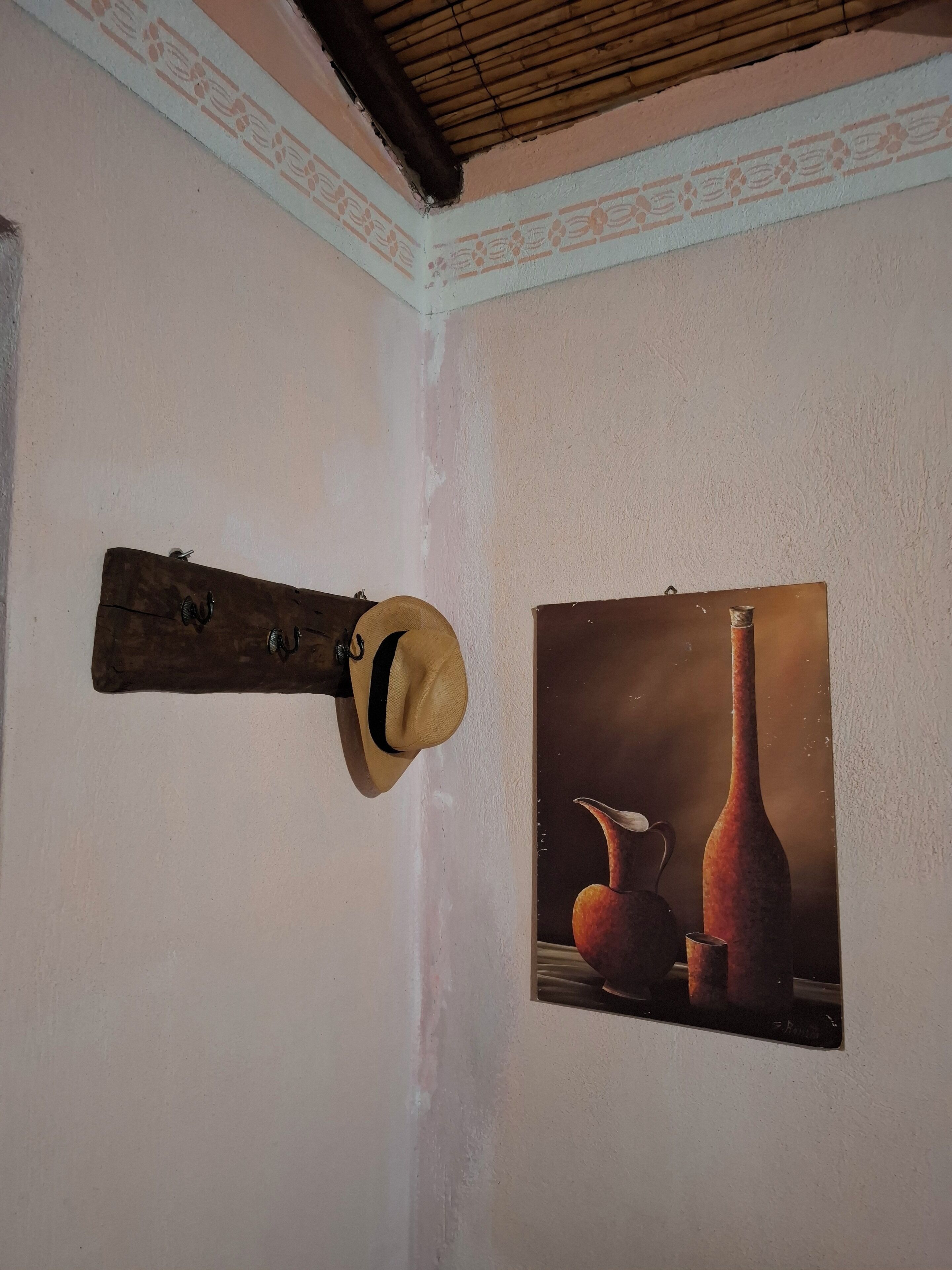 Ein Zimmer mit einem hölzernen Wandhaken, einem gerahmten Bild von einer Vase und einem Krug, sowie einer Bambusdecke.