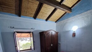 Een kamer met een bed, een kledingkast, een raam en een plafond met houten balken.