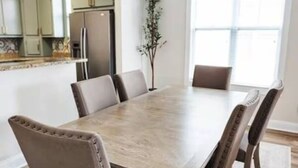 Een eetkamer met een grote houten tafel, gestoffeerde stoelen en een hanglamp.