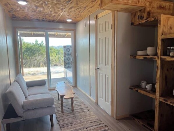 A room with a grey sofa, a small table, and a wooden cabinet with shelves.
