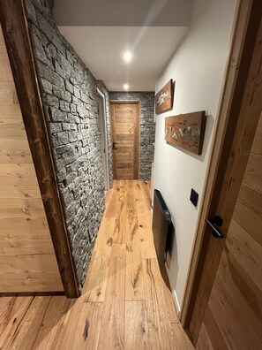 Un pasillo con suelo de madera, pared de piedra y puerta de madera.