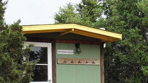 Eine hölzerne Struktur mit gelbem Dach, beschriftet als "Persimmon House", mit einer Holzterrasse und einer kleinen Veranda.