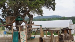 A playground with a slide, climbing wall, and wooden play structures. - Pine Tiny House Rental (Bandera)