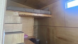 A compact room with a bunk bed, wooden cabinets, and a small window. - Sage Brush Tiny House (Bandera)